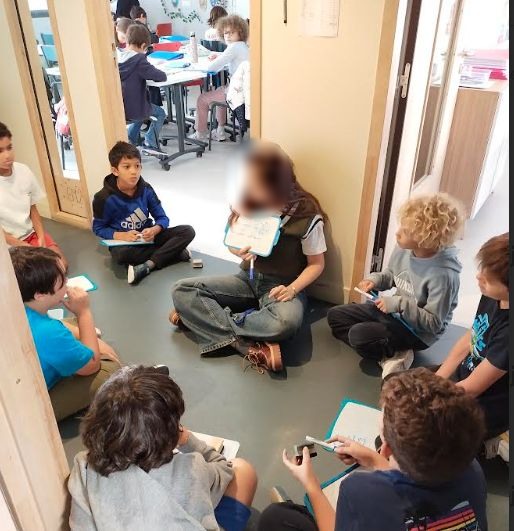 Une enseignante accompagne un petit groupe dans le couloir avec des ardoises